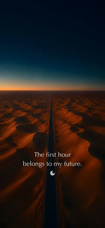 Morning affirmations wallpaper — dawn aerial photograph of one empty road running straight across a deep orange dune field toward the pre-dawn horizon, with the affirmation 'The first hour belongs to my future.' in serif type.