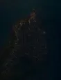 Dawn aerial photograph: a coastal town still asleep before dawn, one window lit at its edge.