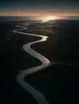 Dawn aerial photograph: a river winding across a dark plain toward the sea at first light.