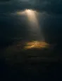 Dawn aerial photograph: a shaft of first light breaking through clouds onto a single patch of dark valley.