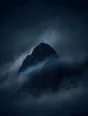 Dark elemental photograph: a solid dark peak in a sea of dusk fog, one fog current dissolving into faint teal marks as it streams past.