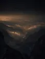 Dark elemental photograph: a high golden hour overlook above a deep valley, the route below catching last light and dissolving into glowing marks at its farthest bend.