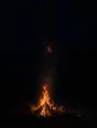 Dark elemental photograph: a small campfire on black sand at night, its rising sparks resolving into small glowing marks.