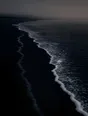 Dark elemental photograph: two foam tide lines on black sand at grey dawn, the fresh higher line still forming as faint silver marks.