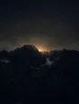 Dark elemental photograph: a jagged ridge before sunrise, pale gold light gathering behind the summit and dissolving into small glowing marks.