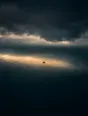 Dawn aerial photograph: a single boat riding a band of first light on a dark sea under storm clouds.