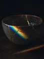 Refracted-light photograph: a gold-repaired ceramic bowl on dark wood, its seams catching refracted light.