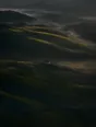 Dawn aerial photograph: misted green hills at dawn with a single farmhouse, its window lit.