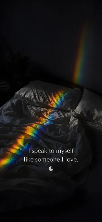 Self-love affirmations wallpaper — refracted-light photograph of a band of refracted spectral light lying across the rumpled linen of an unmade bed in a dark room, with the affirmation 'I speak to myself like someone I love.' in serif type.