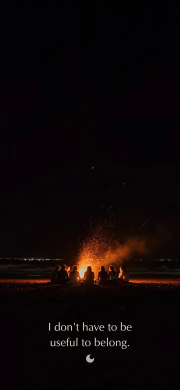 Affirmations for men wallpaper: night photograph of men sitting together around a fire on a dark beach, sparks lifting into a black sky, with the affirmation 'I don't have to be useful to belong.' in serif type.