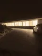 Struck-light photograph: a long modern house on a dark hillside at night, its window band lit end to end, one car parked close against it on the gravel