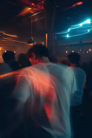 Motion photograph: a man dancing at the back of a crowded room at night, the room's lights swinging around him
