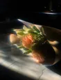Prism-light photograph: Cut flowers still wrapped in their paper on a kitchen counter, hard sun driving through the petals and leaves.