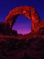 Film photograph: a grand red-rock arch glowing at dusk, deep violet sky showing through the opening.