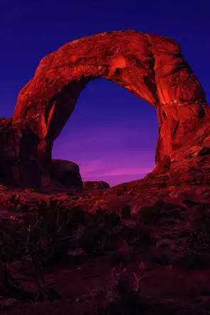 Film photograph: a grand red-rock arch glowing at dusk, deep violet sky showing through the opening.