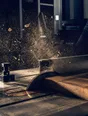 Motion photograph: a table saw driving through hardwood in a bright workshop, a dense plume of sawdust lit hard from behind