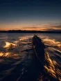 Motion photograph: a rowing eight mid-stroke on open water at first light, the blades catching and throwing water lit from behind