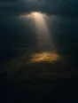 Dawn aerial photograph: a shaft of first light breaking through clouds onto a single patch of dark valley.