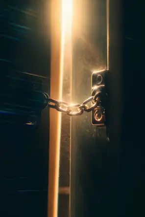 Prism-light photograph: A door chain drawn across a narrow gap in a door, dust drifting in the lit air of the gap.