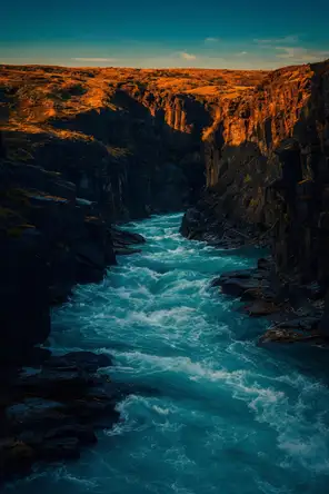 Film photograph: a river in full spring flood pouring turquoise through a narrow dark canyon at evening.
