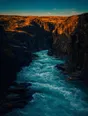 Film photograph: a river in full spring flood pouring turquoise through a narrow dark canyon at evening.