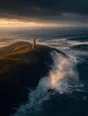 Dawn aerial photograph: storm surf bursting gold against a dark rock headland, a small stone lighthouse holding the point.