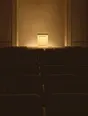 Struck-light photograph: an empty auction room at dusk, rows of chairs in flat silhouette against one lit podium