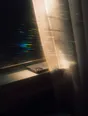 Prism-light photograph: A phone lying face down on a windowsill behind a half-drawn sheer curtain.