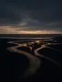 Dark elemental photograph: braided river channels crossing black sand toward a dark sea at dusk, the newest channel in the foreground rendering as glowing amber marks.