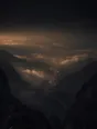 Dark elemental photograph: a high golden hour overlook above a deep valley, the route below catching last light and dissolving into glowing marks at its farthest bend.