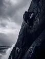 Motion photograph: a climber high on a wet sea cliff under a breaking storm, spray blowing across the rock from the surf below