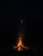 Dark elemental photograph: a small campfire on black sand at night, its rising sparks resolving into small glowing marks.
