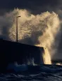 Motion photograph: a harbour breakwater taking a heavy wave head-on at storm dawn, the water exploding vertically up the wall
