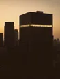 Struck-light photograph: dark glass office towers at dusk with one single floor near the top fully lit and every other floor black