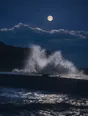 Film photograph: a full moon over a king tide breaking high against a dark sea wall, backlit spray in indigo and silver.