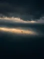 Dawn aerial photograph: a single boat riding a band of first light on a dark sea under storm clouds.