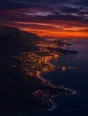 Film photograph: an aerial view of a dusk coastline where dark mountains, a glowing city, and the open sea meet.