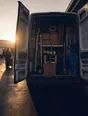 Dark cinematic photograph: The open back of a small trade van with everything in its place and everything within reach, morning light flooding in.