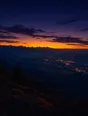 Film photograph: dawn breaking gold behind a dark mountain range while the valley below still sparkles with night lights.