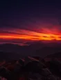Film photograph: a summit panorama at sunset, the whole horizon burning crimson and gold above dark ridgelines.