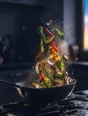 Motion photograph: a pan of vegetables tossed over a home hob at dusk, everything airborne and lit hard from the side