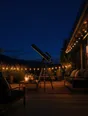 Film photograph: a terrace at night strung with warm fairy lights, a telescope pointed at a sky full of stars.