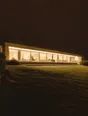 Struck-light photograph: a long low modern house on a dark hillside at night, its whole window band lit from end to end