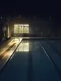 Dark cinematic photograph: An empty swimming lane at dawn, the water dead still, the hall dark above.