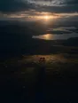 Dawn aerial photograph: a lone weathered bench on a hilltop facing the sunrise, dew on the grass.