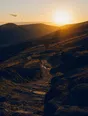 Dark cinematic photograph: A wide hillside path at golden hour with one walker far off and small.