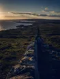Dark cinematic photograph: A hand-built stone wall running away across open country, hard side light on every stone.