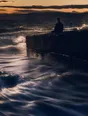Motion photograph: a man sitting on a sea wall at dusk watching the tide run hard below him