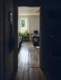 Dark cinematic photograph: A doorway seen from a dark hall into a bright room, the same floorboards running through both.