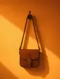 Grainy gradient illustration: One small leather satchel hanging on a hook on a warm sunlit wall, nothing else on the wall.